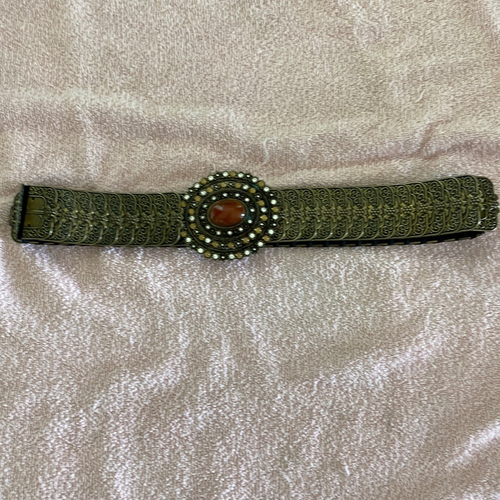 Metal chain link style belt with hook closure and round beaded buckle. Stretch.